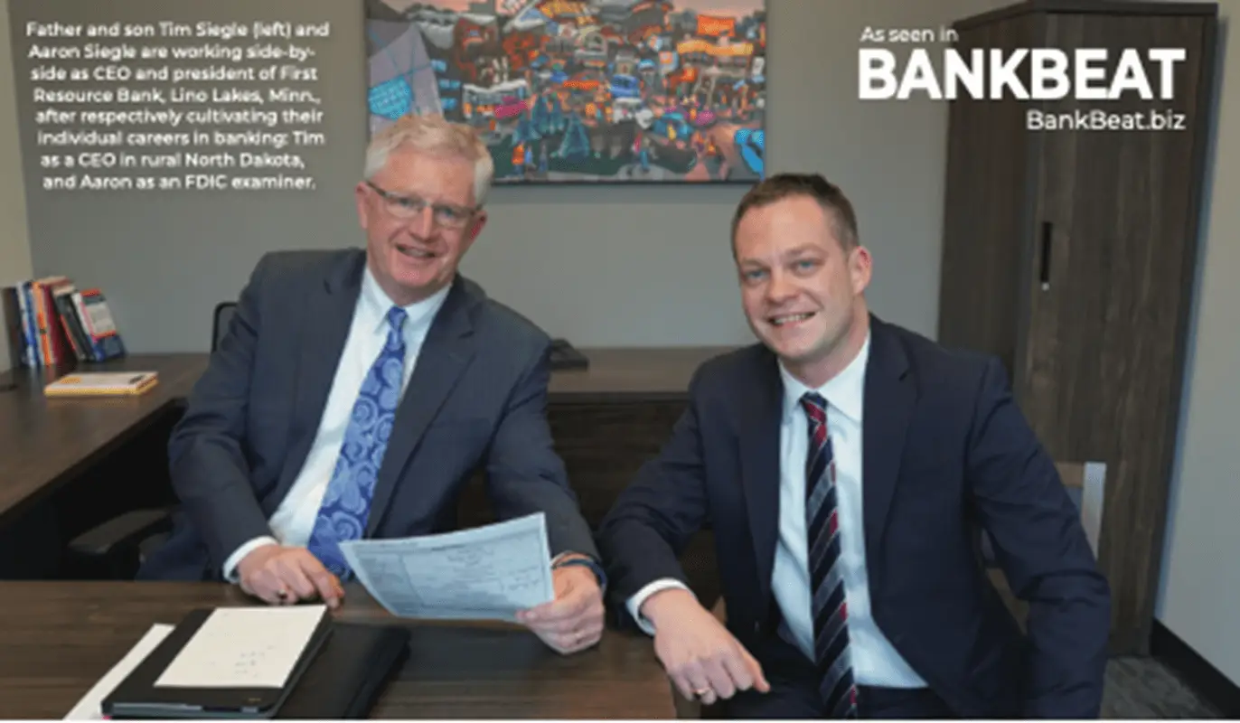 two men in suits sitting at a desk